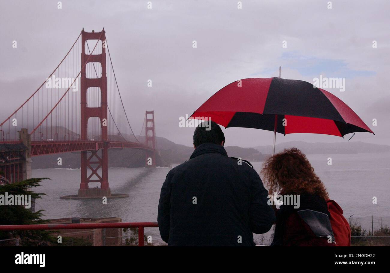 Tourists with umbrella viewing Golden Gate Bridge in rainy weather