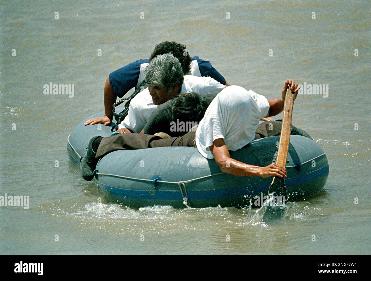 A Mexican man hides his face from the camera as he rows his raft with ...