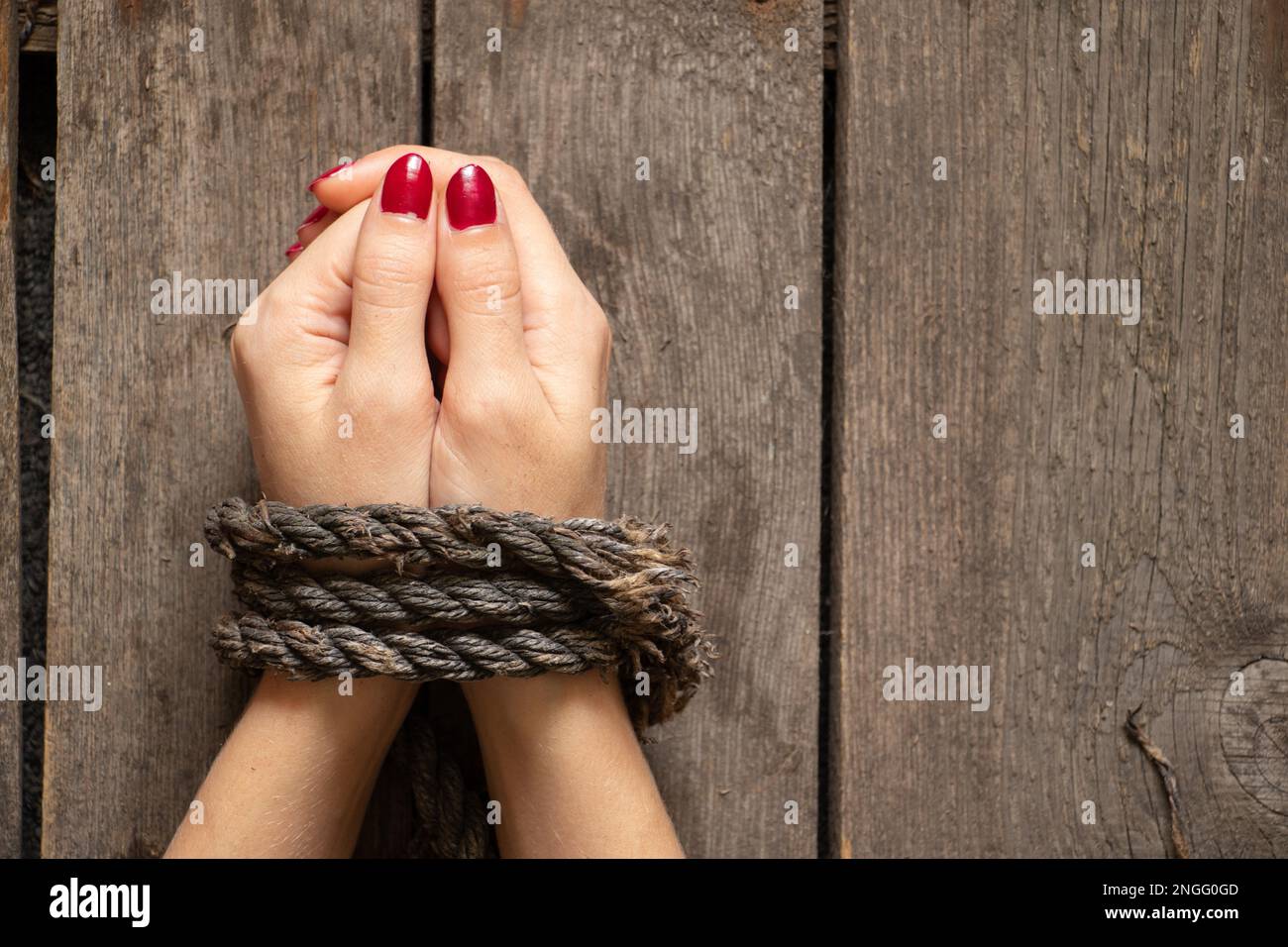 tied female hands with rope on wooden background close up Stock Photo