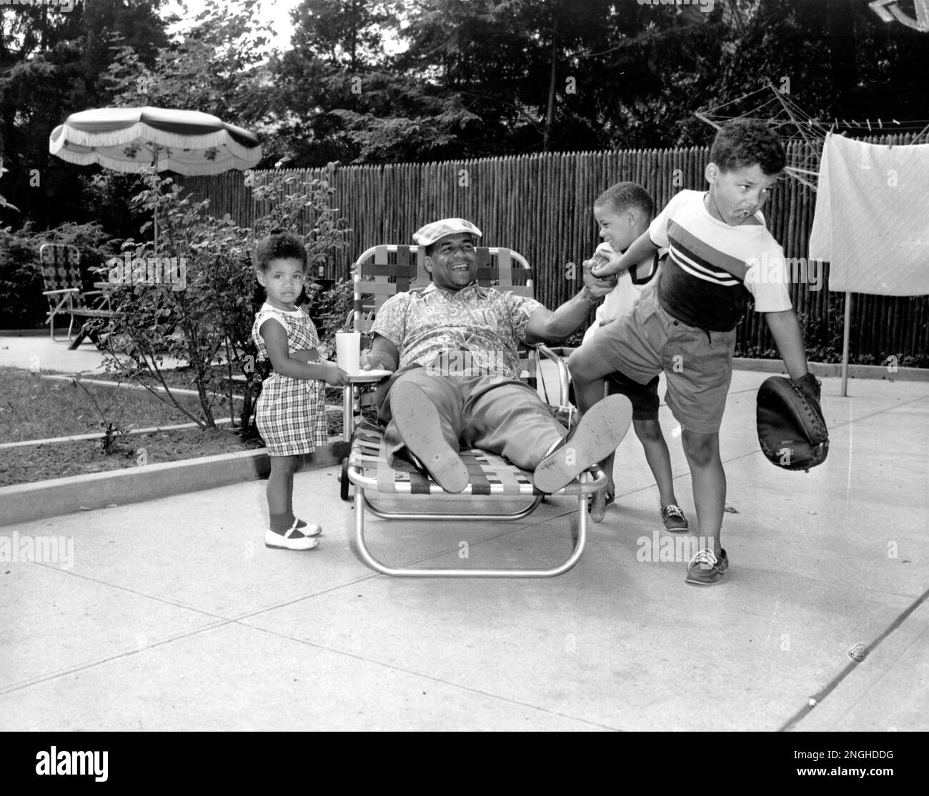 Brooklyn Dodgers catcher Roy Campanella, who is out with an injured knee,  is being persuaded by his sons, Tony, 5, and Roy Jr., 7, right, to play  baseball in their backyard in
