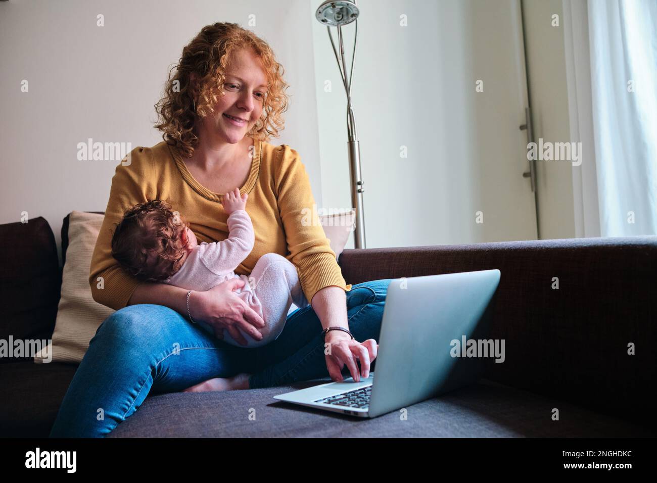 Woman breastfeeding her baby while working with a laptop on the sofa at home Stock Photo Alamy