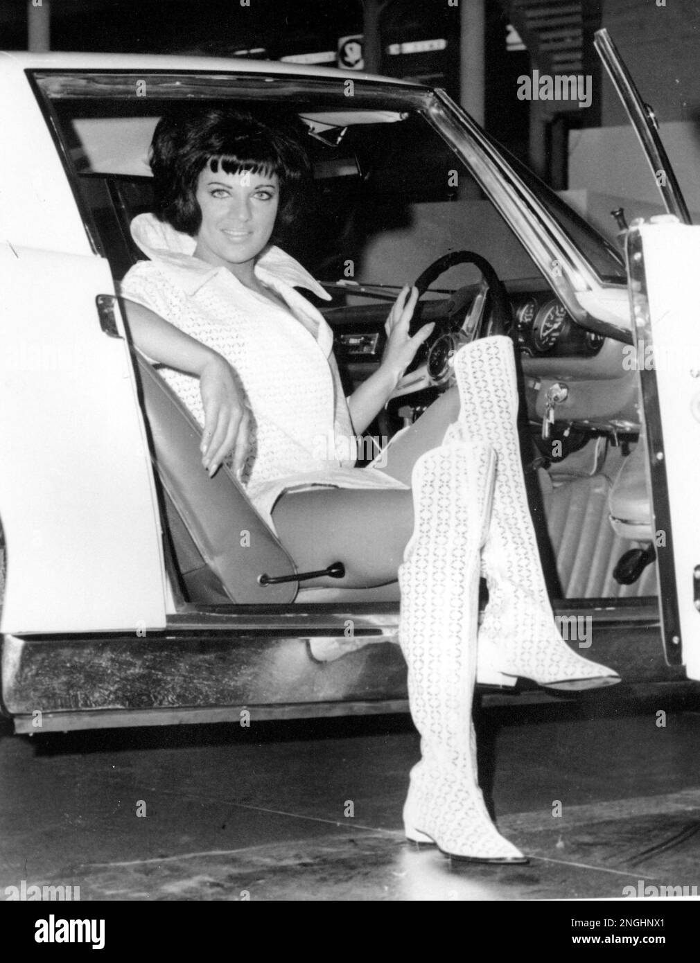 Rita Romano, an Italian model, poses in the driver's seat of a car wearing a mini dress of