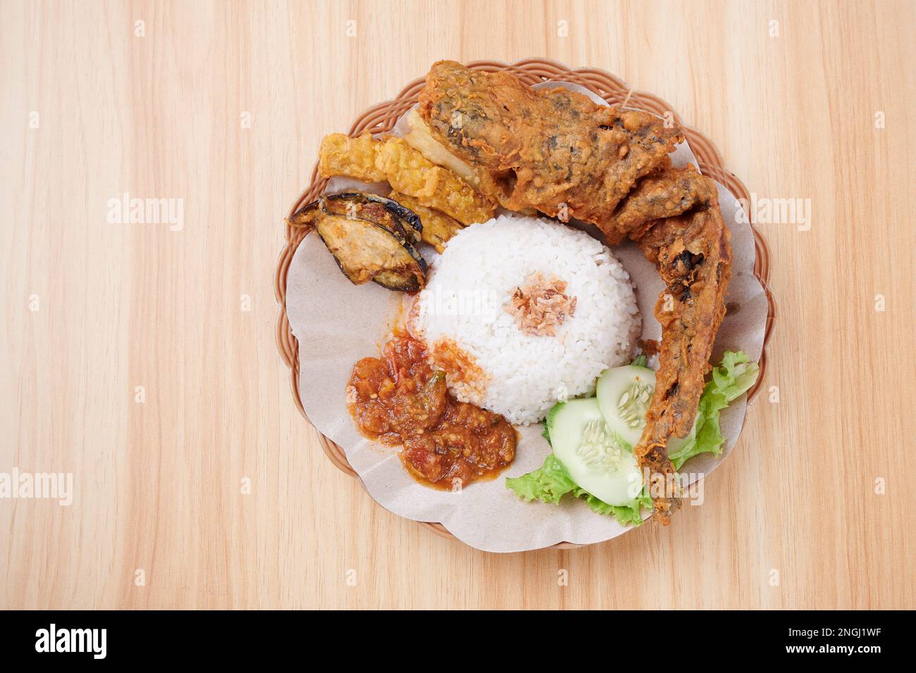 Fried Catfish with Spicy Sauce, rice and vegetables on a plate (Pecel Lele) Stock Photo