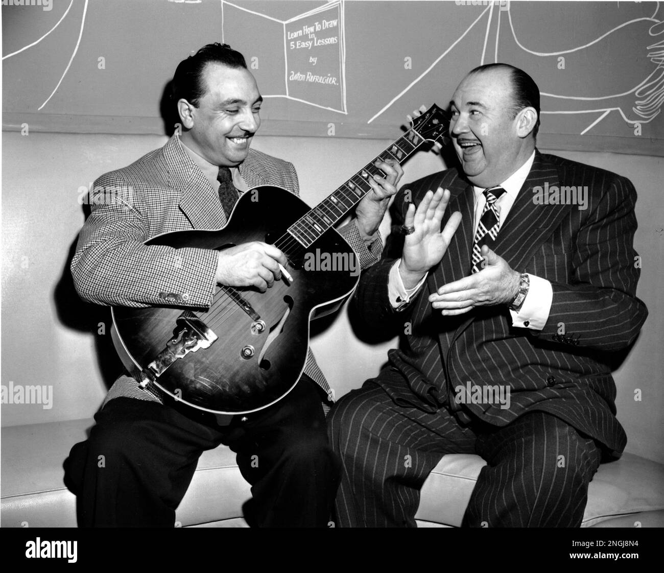 Jazz guitar virtuoso Django Reinhardt, the "Belgium Gypsy," demonstrates his technique to "King of Jazz" Paul Whiteman at Cafe Society Uptown in New York, Dec. 19, 1946. Reinhardt, who formed France's popular Quintette of the Hot Club of France, perfected an unusual playing style due to an injury to the fingers of his left hand. (AP Photo) Stock Photo