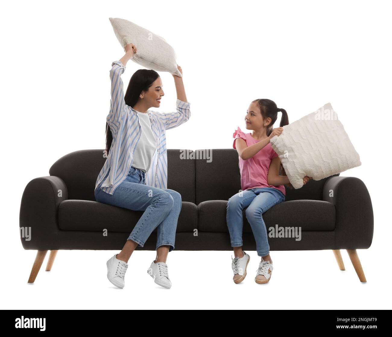 Young woman and her daughter having pillow fight on comfortable grey sofa against white background Stock Photo