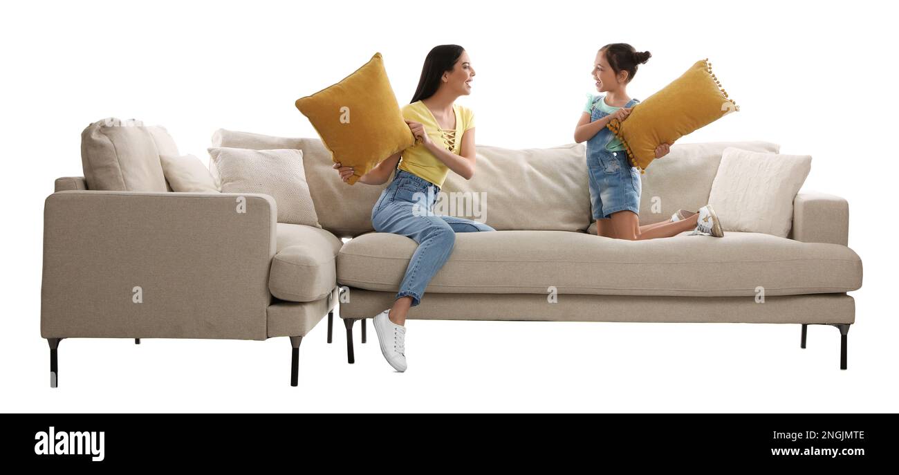 Young woman and her daughter having pillow fight on comfortable sofa against white background Stock Photo