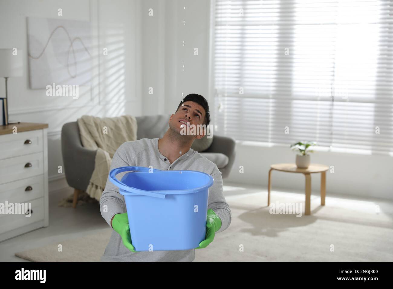 Man collecting water leaking from ceiling in living room. Damaged roof