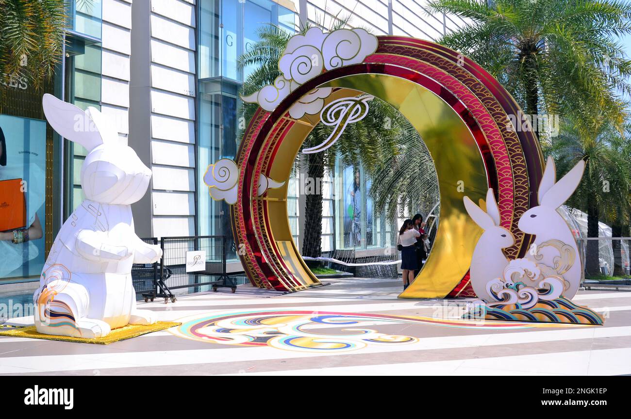 Young women chat beside a Chinese new year display featuring statues of rabbits and a colourful arch outside the Siam Paragon shopping centre or mall, Bangkok, Thailand, Asia. According to the Chinese Zodiac, 2023 is the Year of the Rabbit. Stock Photo
