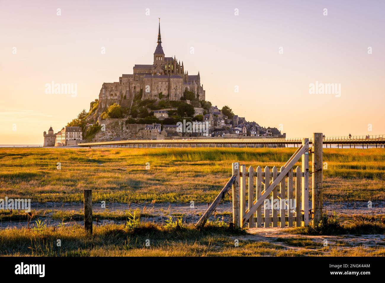 Sunset view of the Mont Saint-Michel tidal island in Normandy, France, with a wooden gate opening onto the salt meadows in the foreground. Stock Photo