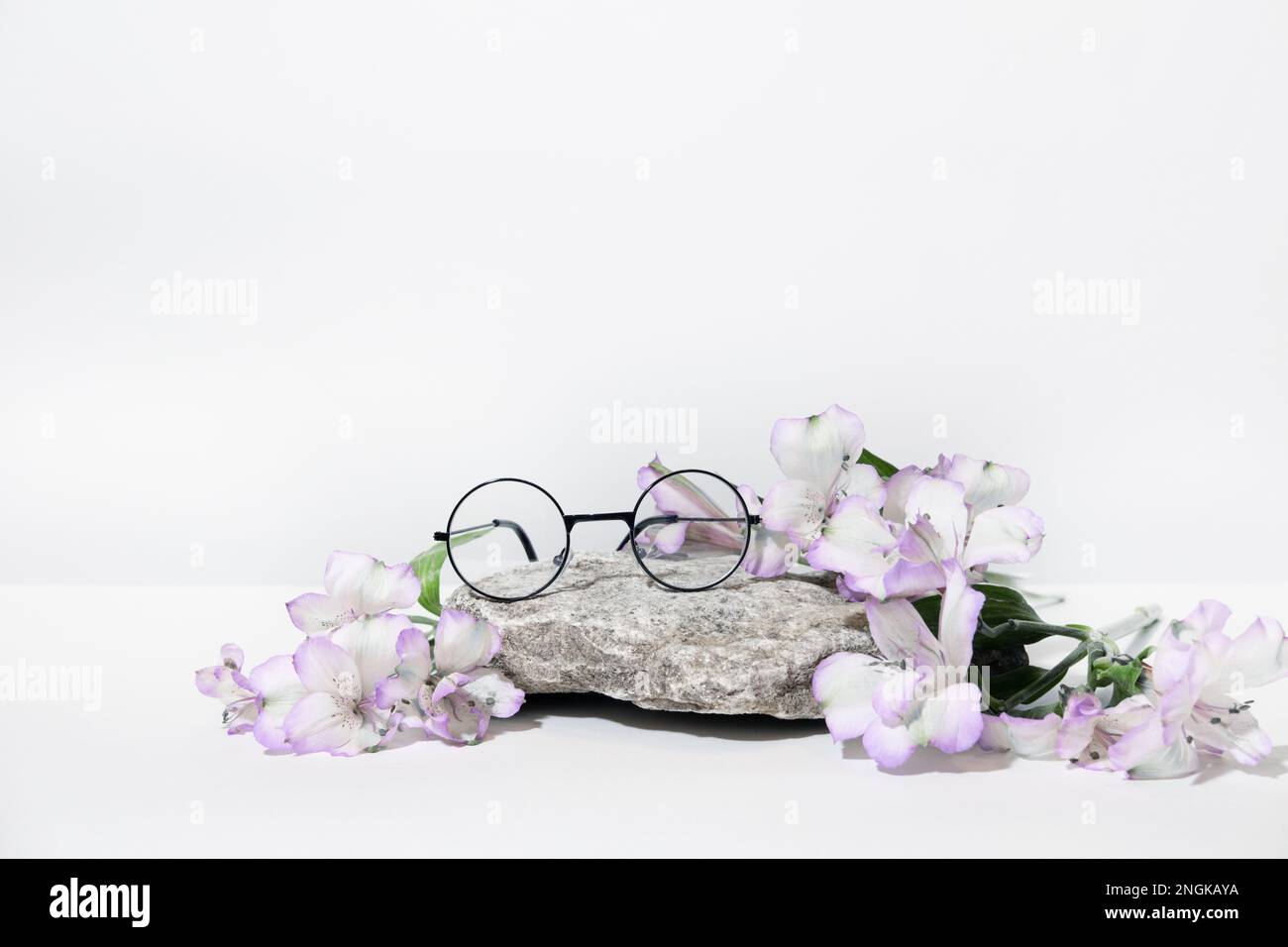 Funny round glasses from the sun or for vision, on a podium stone with pink flowers, on a table, on a white gray background. Creative glasses advertis Stock Photo