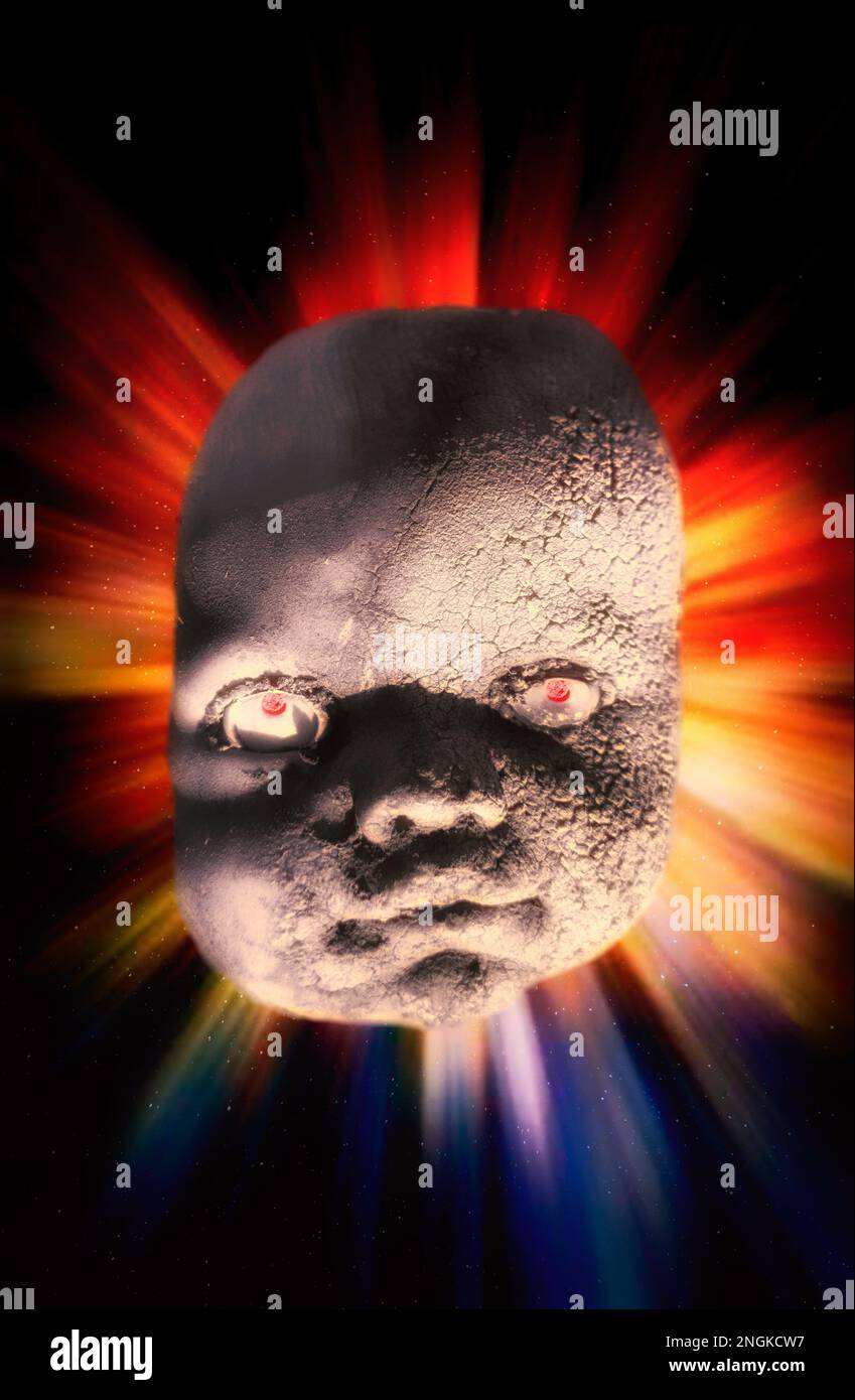 A menacing and bizarre doll's head floating in outer space, in front of a burst of coloured light. Stock Photo