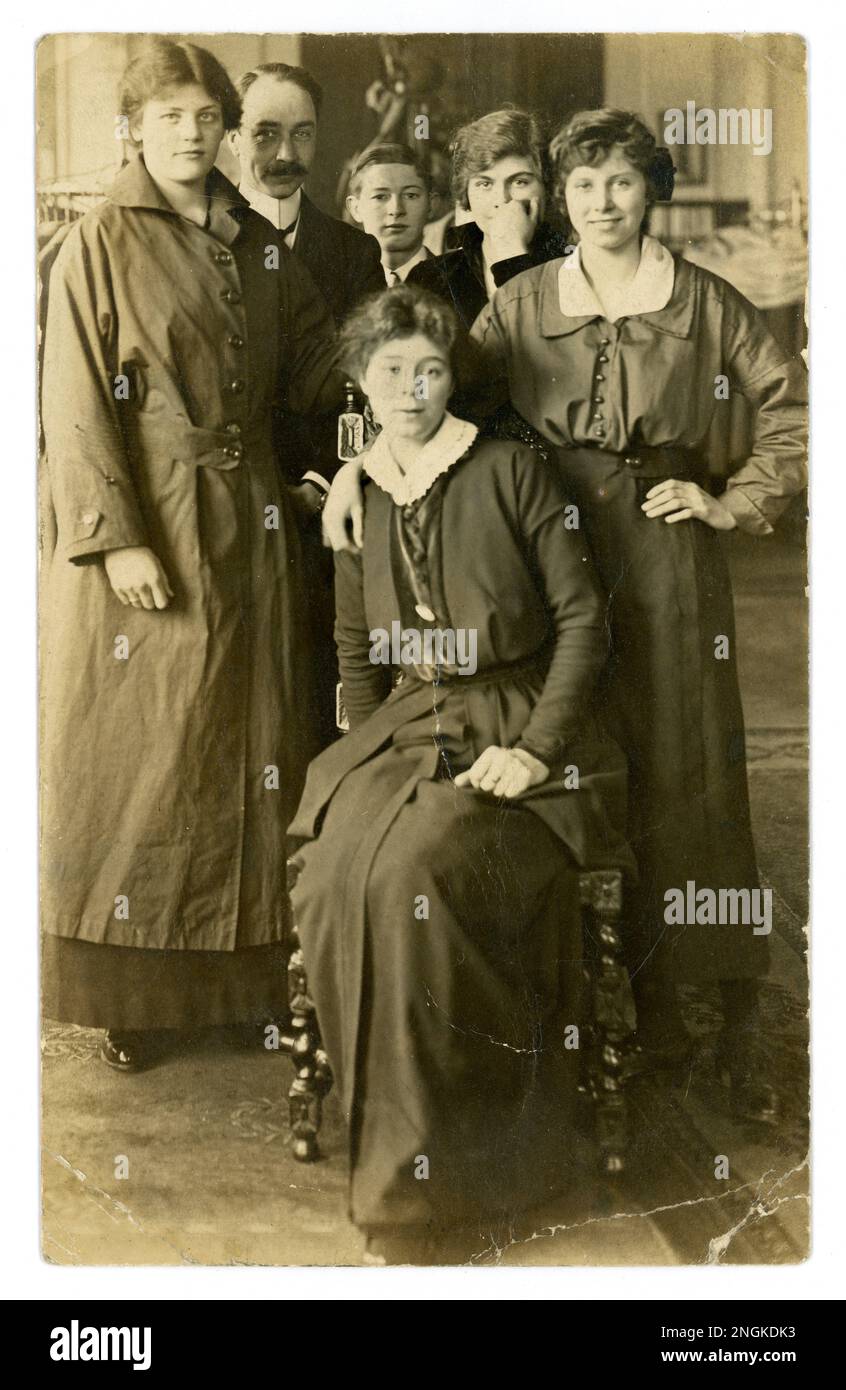 https://c8.alamy.com/comp/2NGKDK3/original-ww1-era-postcard-of-attractive-young-women-possibly-friends-or-sisters-one-is-wearing-work-clothes-of-overcoat-a-boy-and-a-man-look-on-shop-assistant-maybe-family-celebration-wedding-group-in-outfitters-maybe-as-suits-on-hangers-or-is-the-girl-on-the-right-being-fitted-for-a-work-trench-coat-posted-from-tooting-south-london-uk-dated-posted-on-30-april-1915-2NGKDK3.jpg