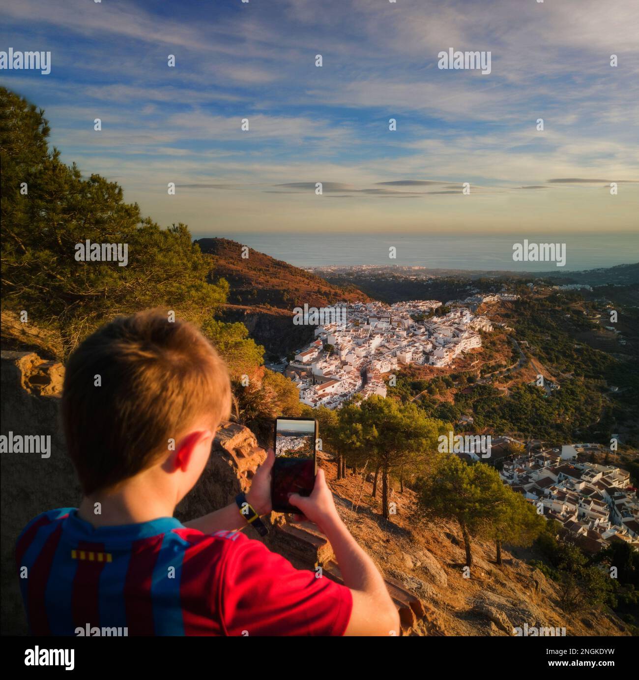 Young boy using a smart phone to photograph Frigiliana Village from above,  Malaga Province, Andalucia, Spain Stock Photo