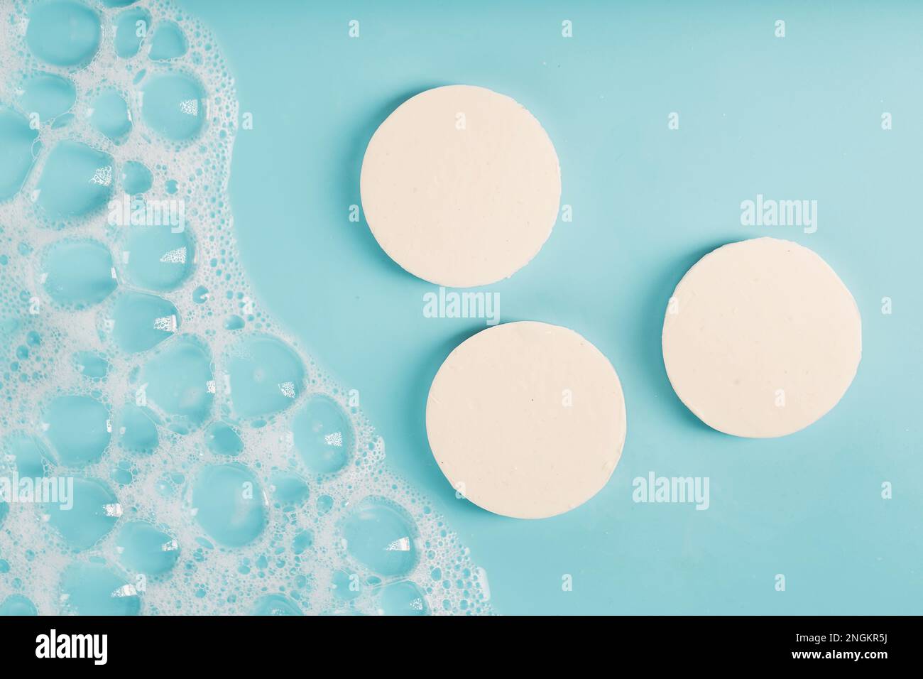 Three round pieces of white soap with foam on a blue background Stock Photo