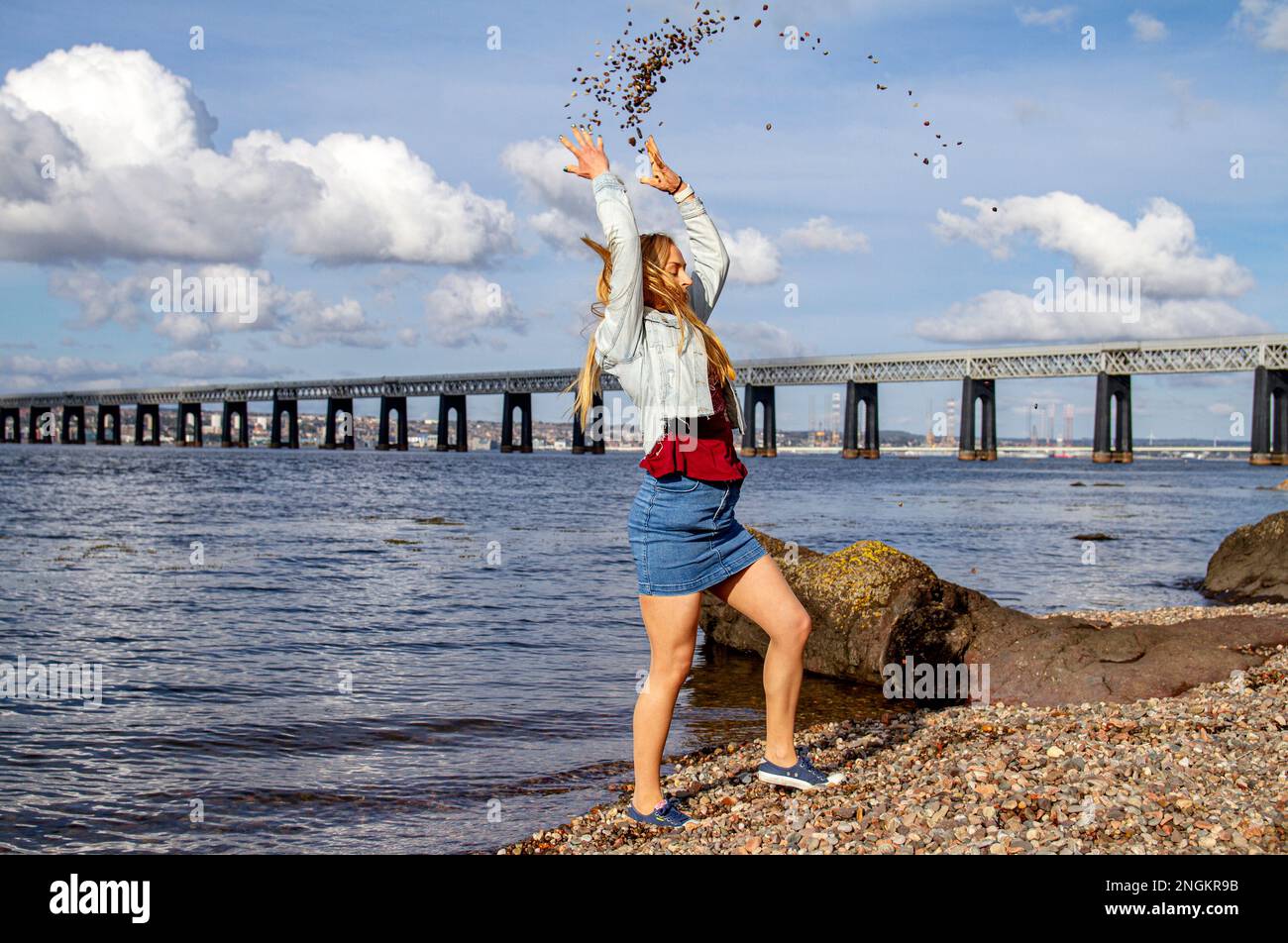 On a beautiful October day in Wormit Beach, Fife, Rhianna Martin throws pebbles over her head into the River Tay, Scotland Stock Photo
