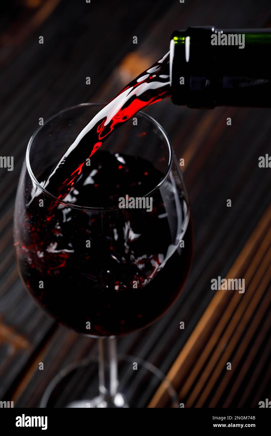 Red wine pouring in glass on wooden table Stock Photo