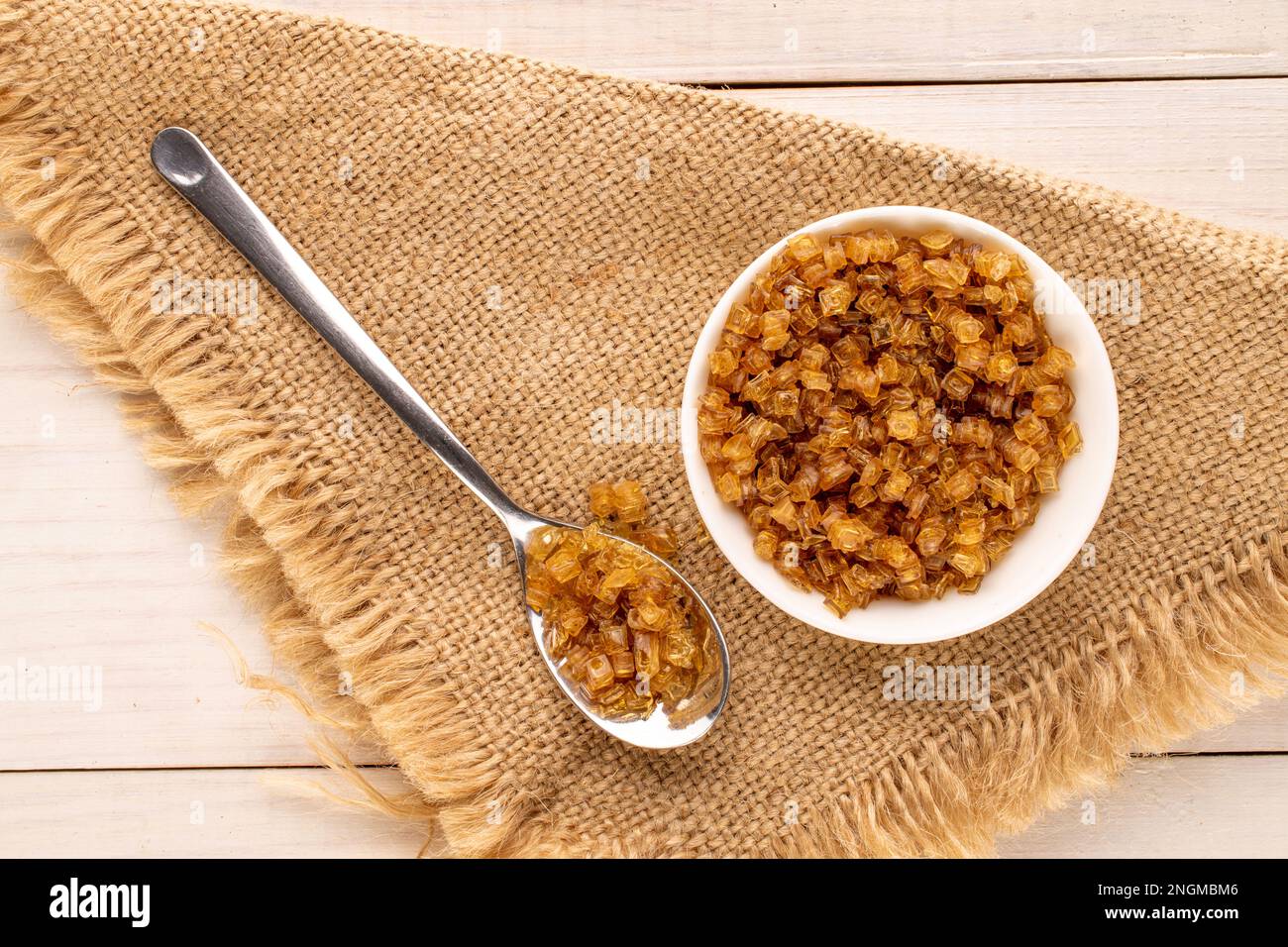 Yellow gelatin granules in white plate with metal spoon and jute napkin on wooden table, macro, top view. Stock Photo