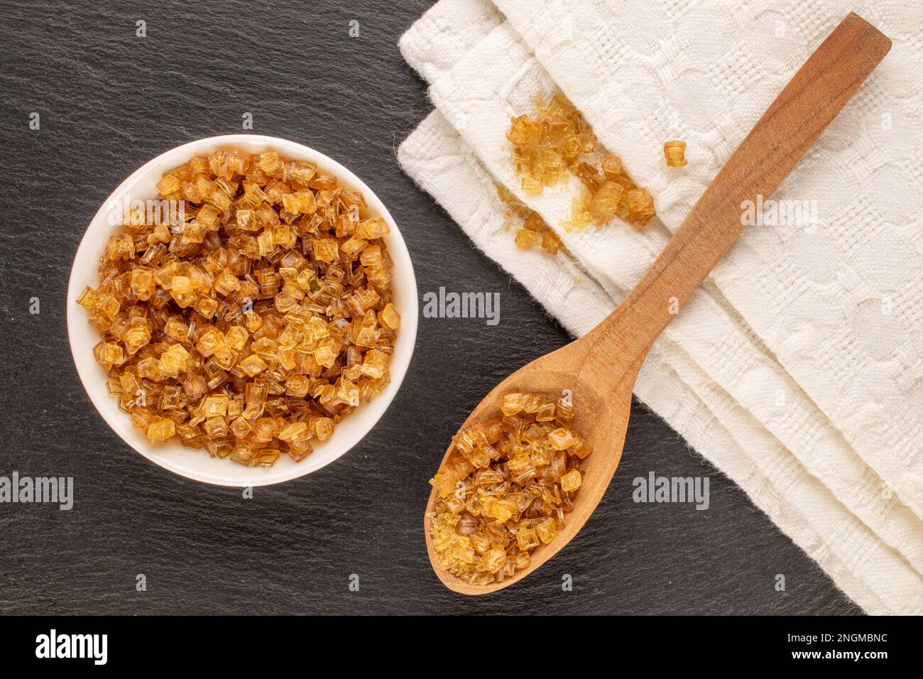 Yellow gelatin granules in white plate with wooden spoon and white napkin on slate stone, macro, top view. Stock Photo