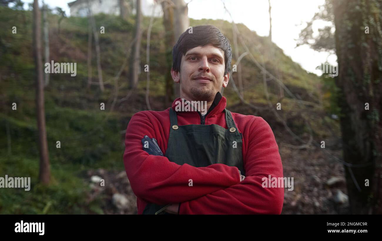 Farmer or Gardener Young Man in Red Dress With Green Apron Smiling Looking at Camera and Crossing Arms, Farmer and Gardener Concept Stock Photo