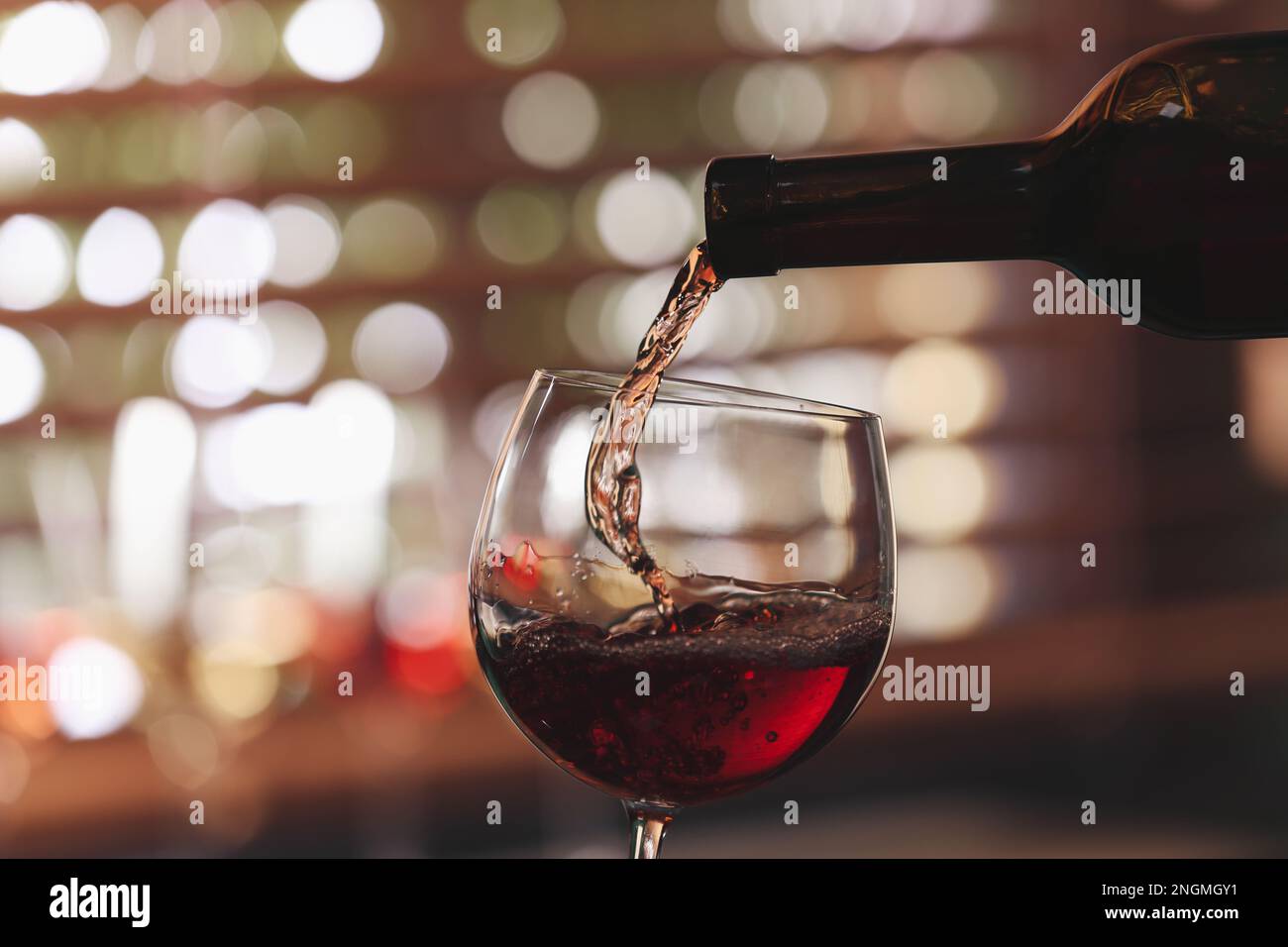 Pouring rose wine from bottle into glass on blurred background, closeup ...