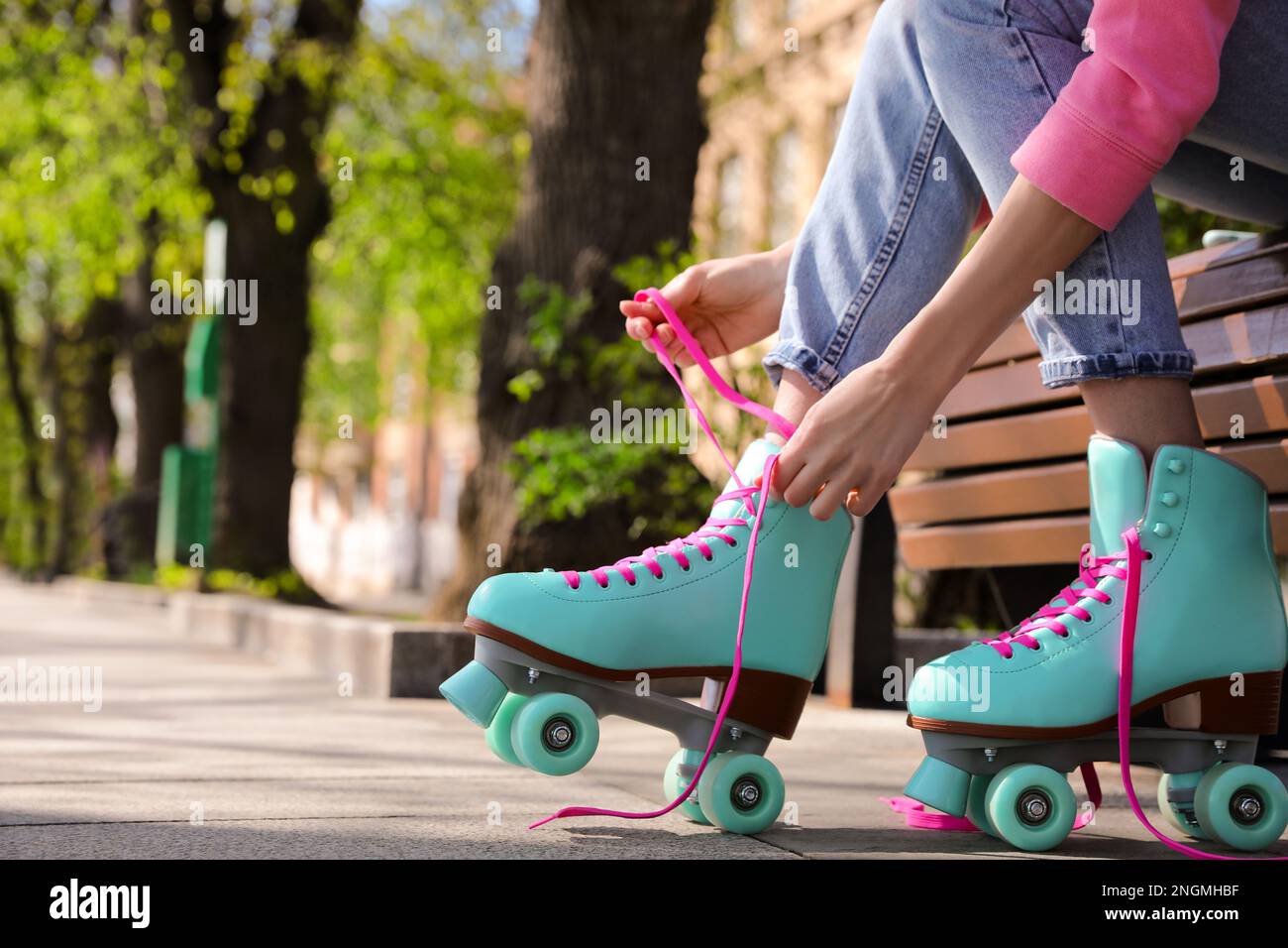Woman lacing roller skates while sitting on bench outdoors, closeup