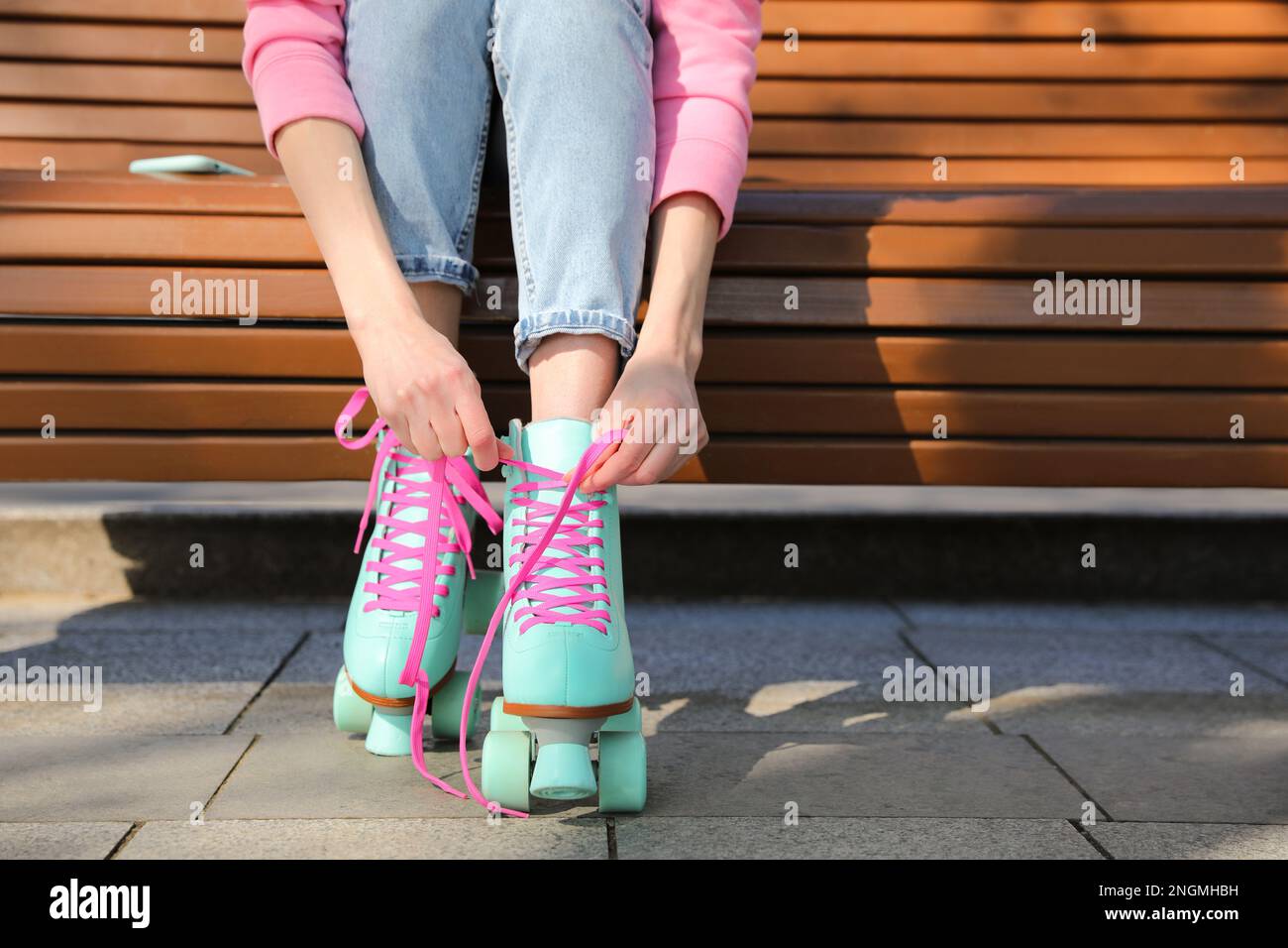 Woman lacing roller skates while sitting on bench outdoors, closeup