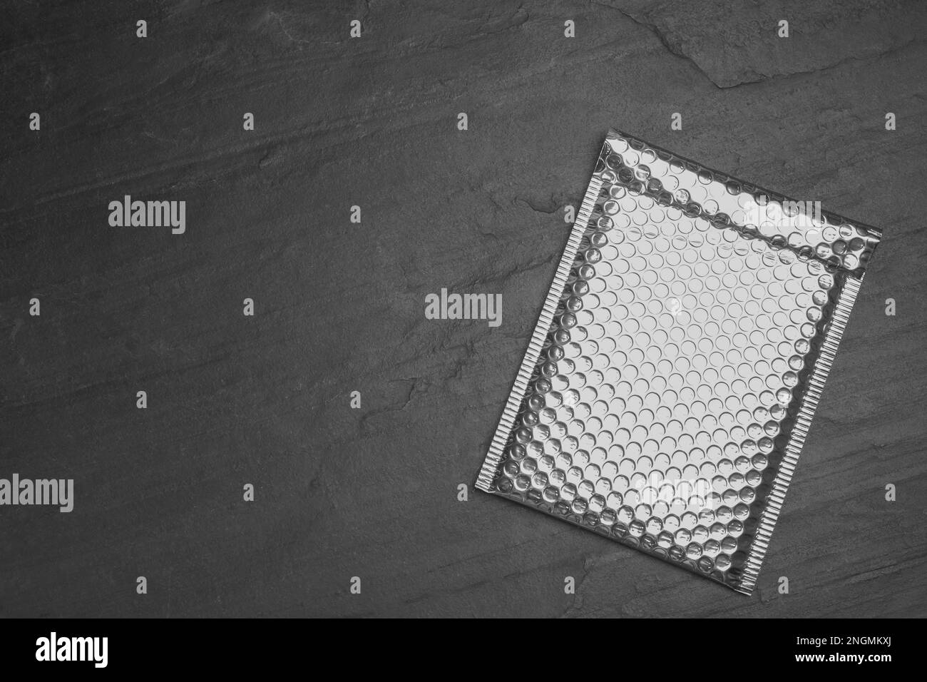 Padded envelope with bubble wrap on black background, top view. Space