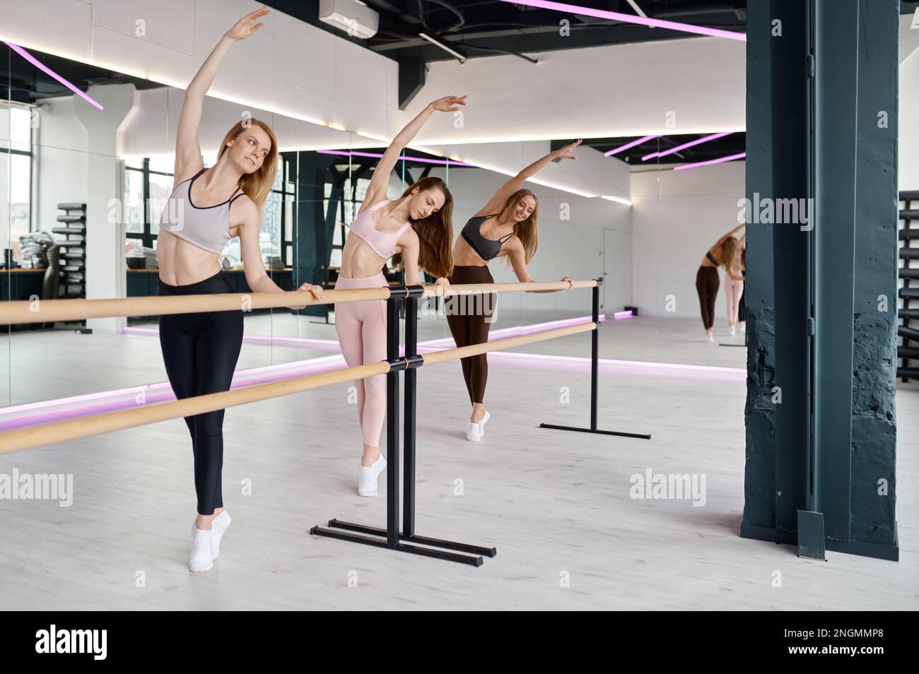 Flexible dancers group practicing ballet moves at ballet bar Stock