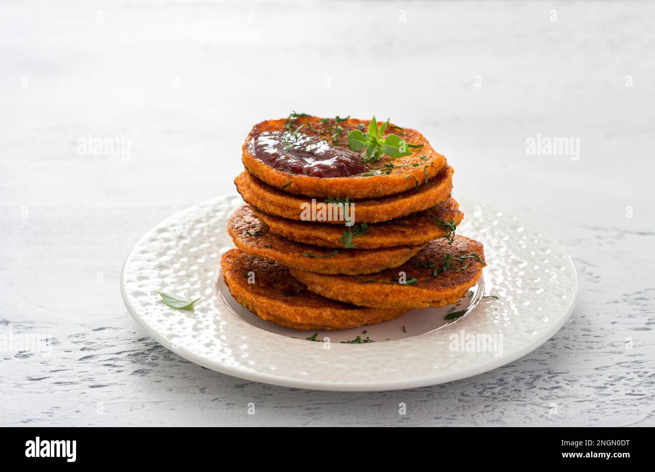 Lentil fritters with plum sauce, tkemali, greens in a white plate on a light blue textured background. Healthy vegan food Stock Photo