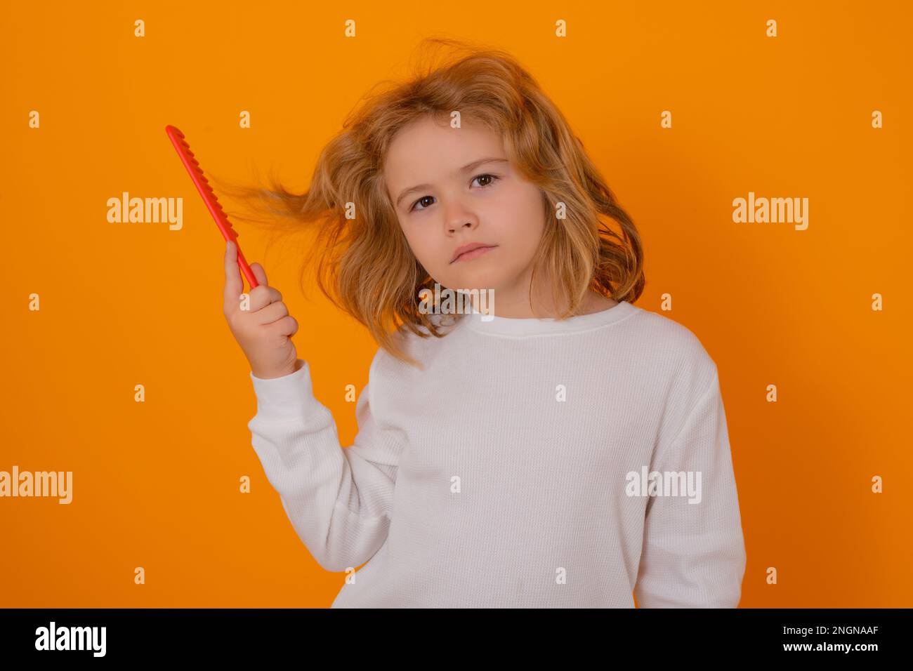Portrait of child combing hair with comb on yellow studio background