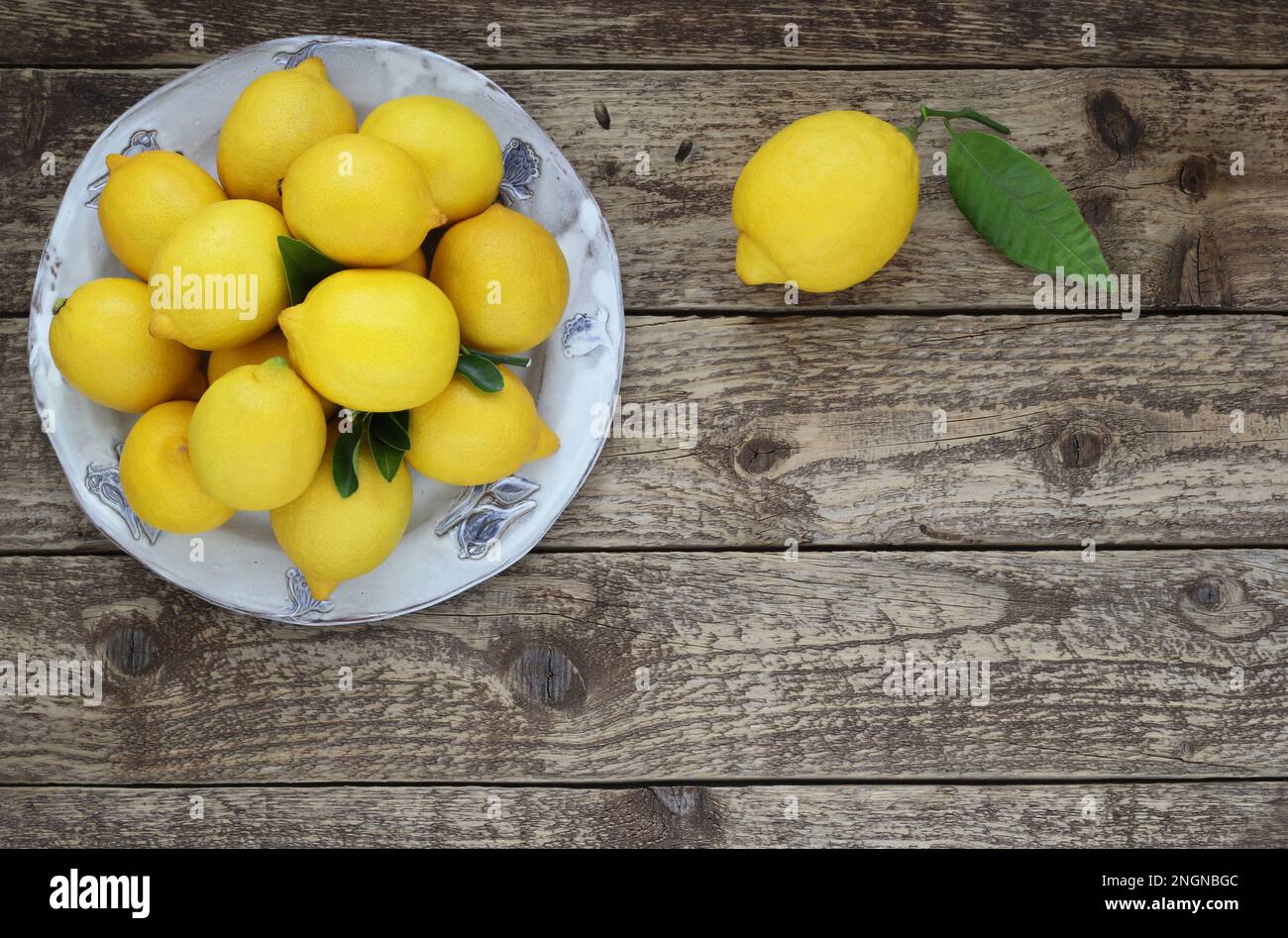 Fresh lemons fruit on a plate on a wooden table. Top view. Decorative arrangement of lemons with leaves on wood background. Stock Photo