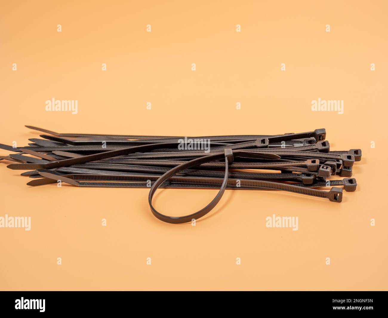 Black plastic cable ties on an orange background. Close-up. Stock Photo