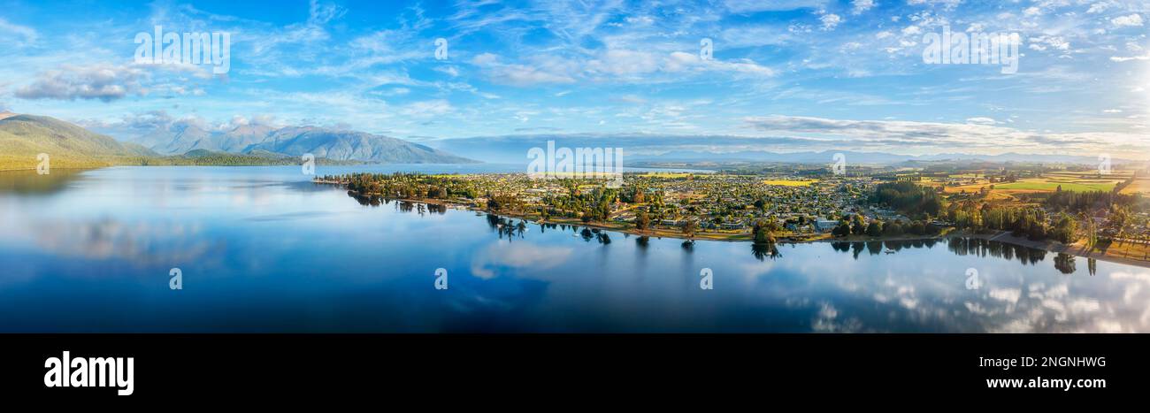 Scenic mount ranges reflecting in calm waters of Te Anau lake and town in Fiordland of New Zealand - gateway to Milford Sound. Stock Photo