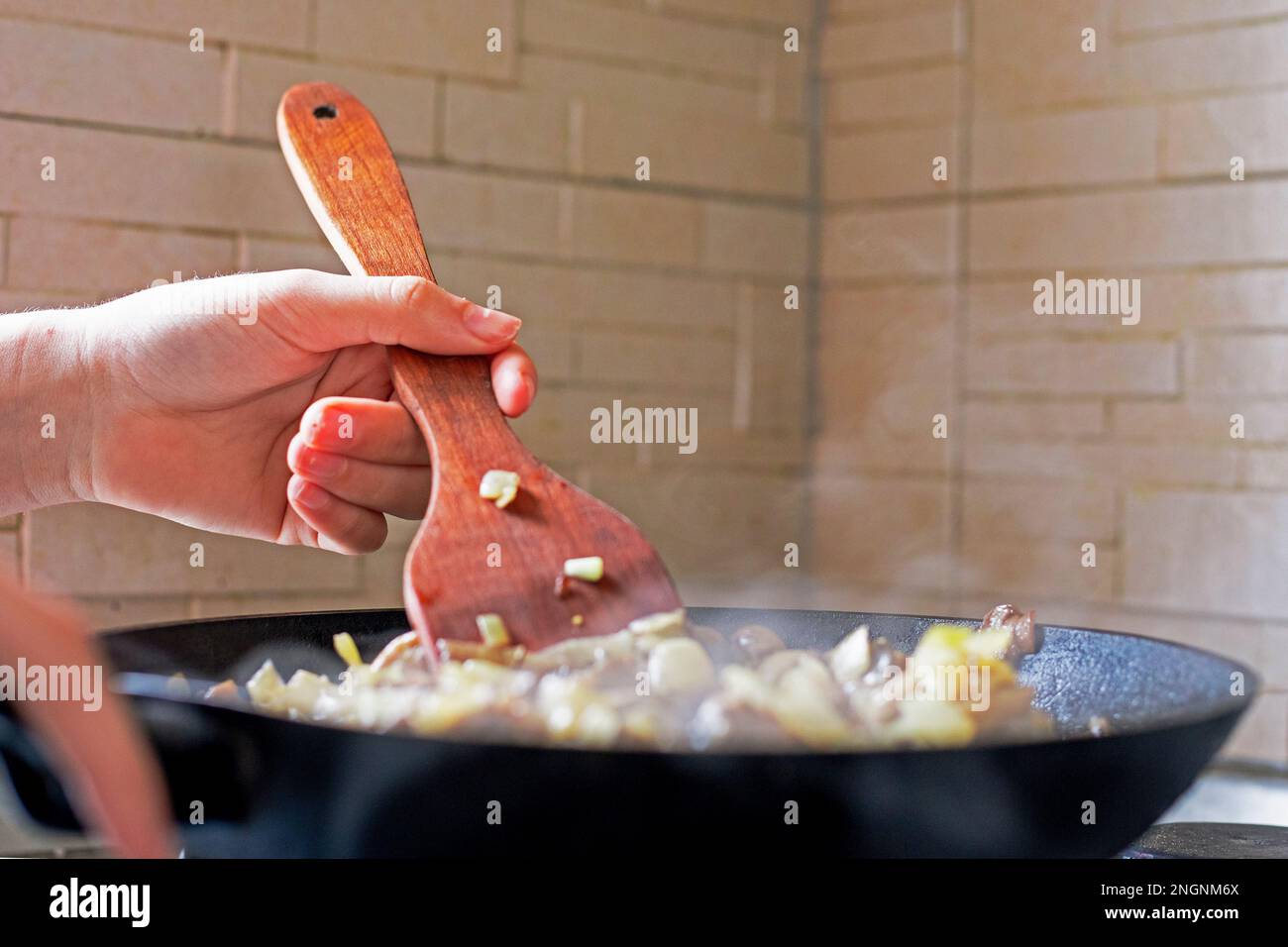 prepare a homemade dinner and mix vegetables and mushrooms in a hot pan with a wooden kitchen spatula. Diet Stock Photo