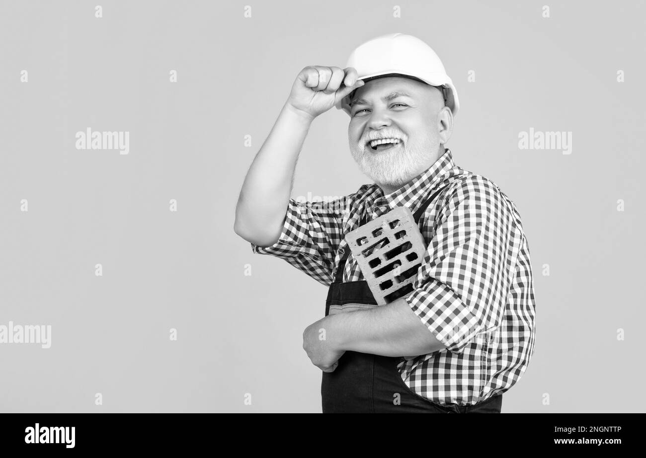 smiling senior man bricklayer in hard hat on yellow background. Stock Photo