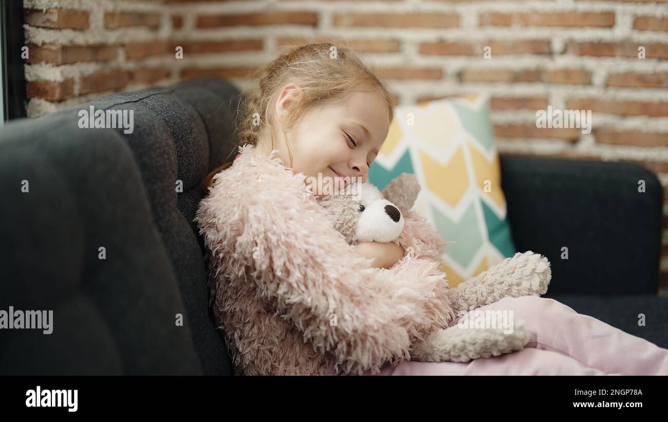 Adorable blonde girl hugging teddy bear sitting on sofa at home Stock ...
