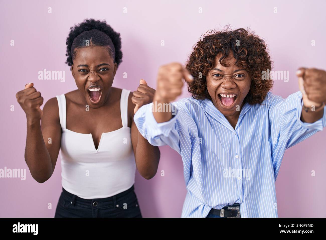 Two african women standing over pink background angry and mad raising ...