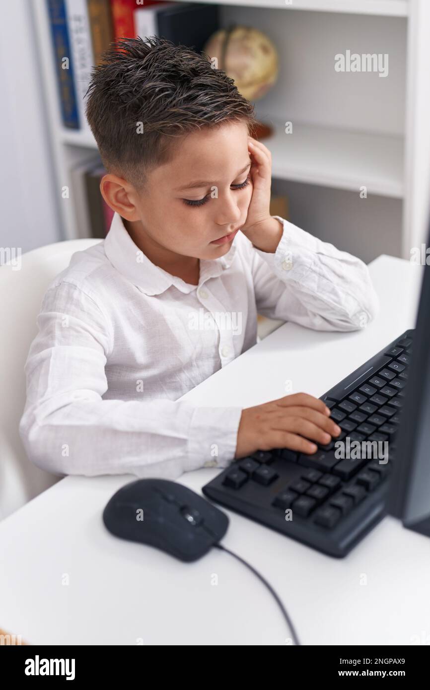 Adorable hispanic boy student using computer with tired expression at ...