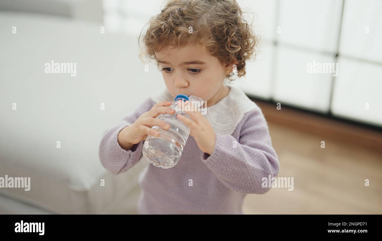 Adorable hispanic girl drinking water standing at home Stock Photo