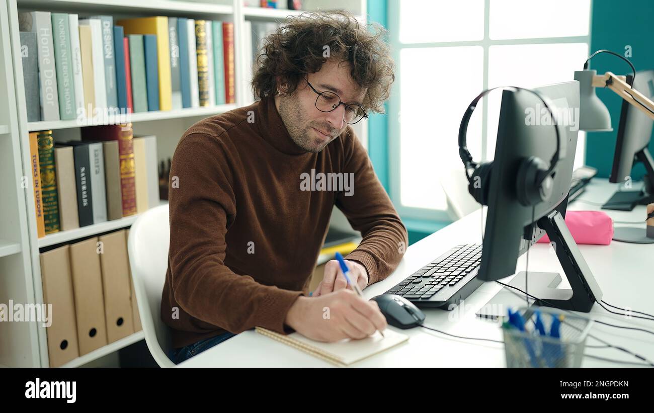 Young hispanic man student using computer writing on notebook at ...