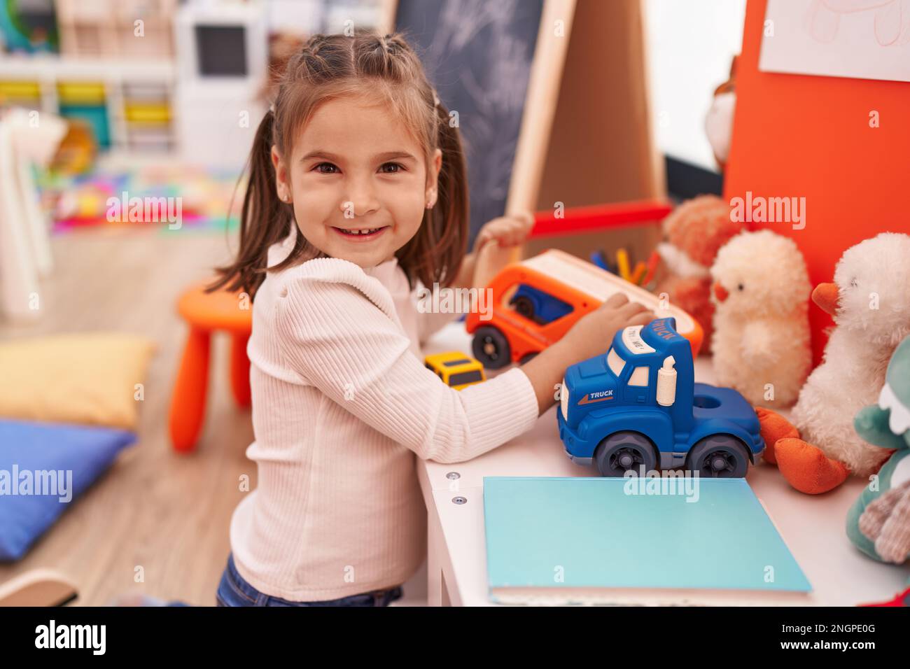 Adorable hispanic girl playing with truck toy sitting on floor at ...