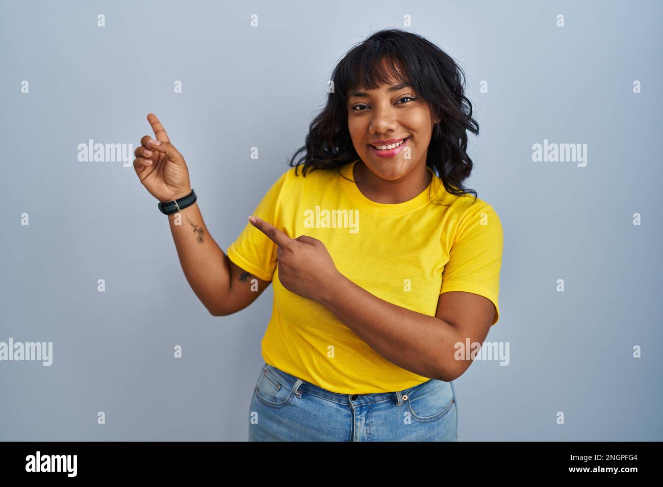 Hispanic woman standing over blue background smiling and looking at the ...