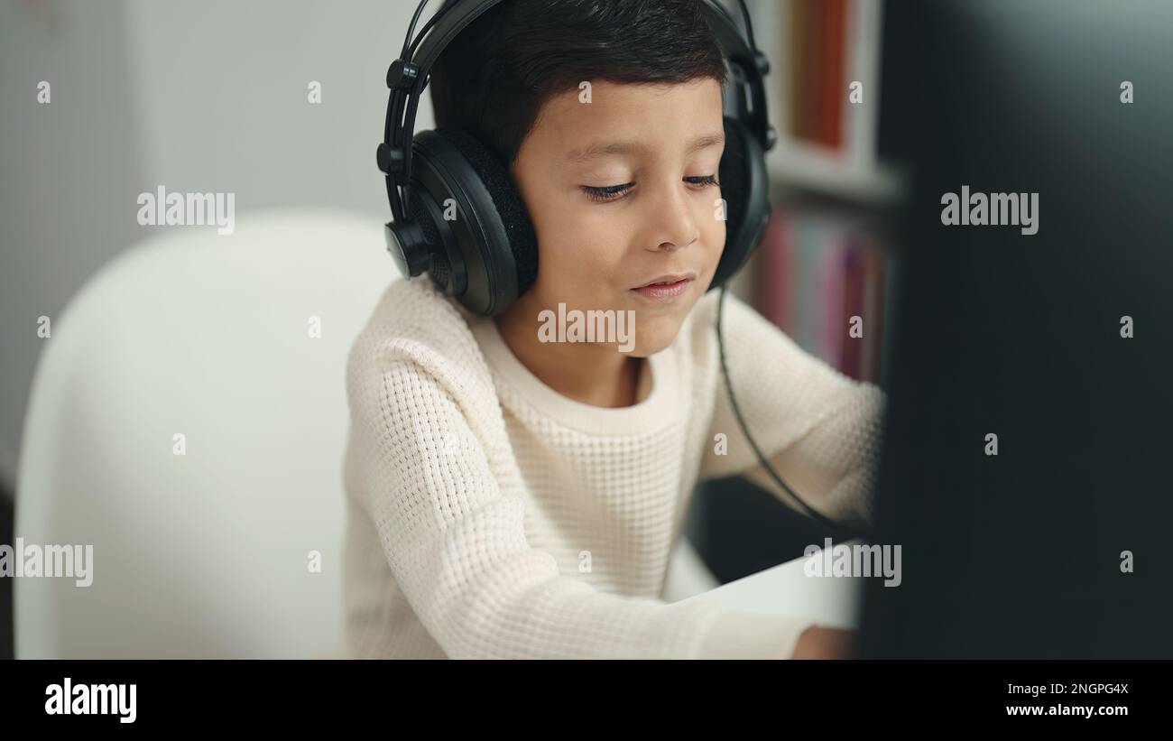 Adorable hispanic boy student using computer sitting on table at ...