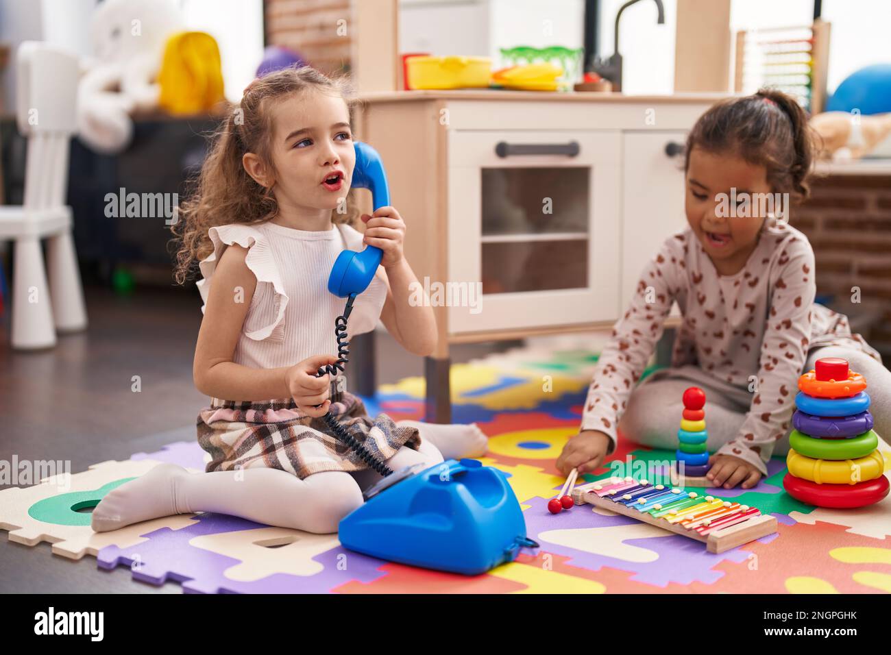 Two kids playing with telephone toy using xylophone sitting on floor at