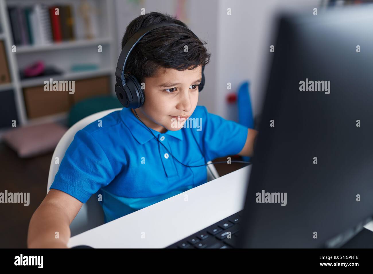 Adorable hispanic boy student using computer sitting on table at ...