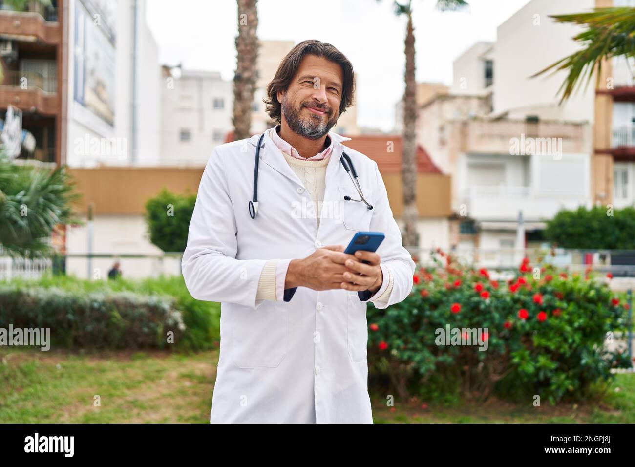 Middle age man doctor smiling confident using smartphone at park Stock Photo
