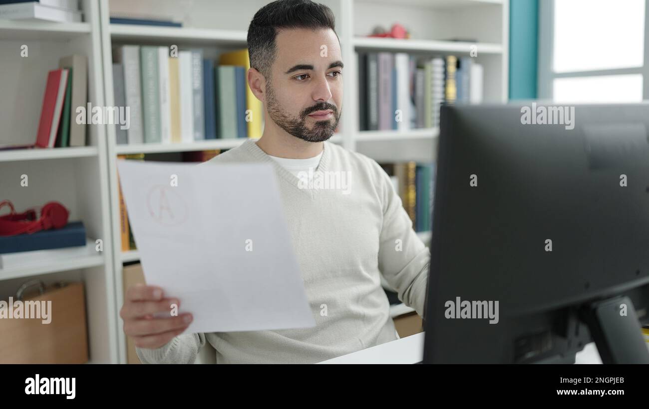 Young hispanic man student using computer reading document at library ...