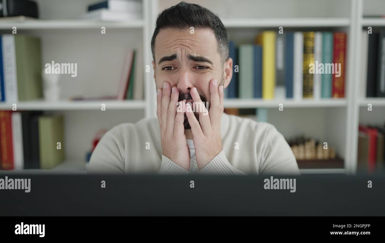 Young hispanic man student using computer stressed at library ...