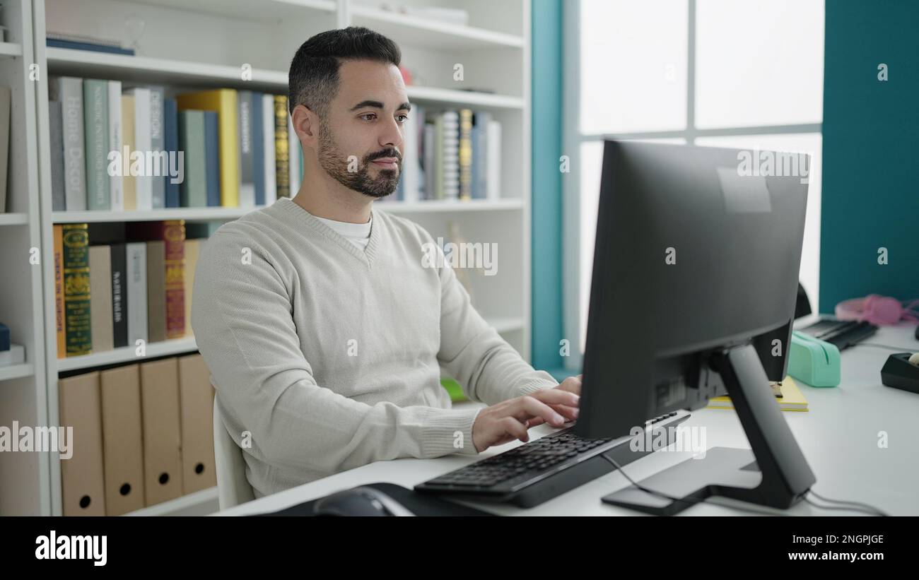 Young hispanic man student using computer studying at library ...