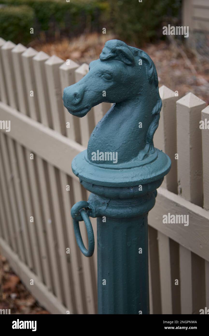 Metallic, green horse hitching post in Connecticut with tan, wooden fence nearby.  This is where you would have tied your horse up, while visiting. Stock Photo